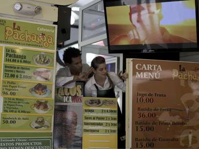 Los empleados Alexey Piedra (izquierda) y Elizabeth Hernández conversan con clientes entre menús con fotos en la cafetería privada "La Pachanga", en La Habana.  Foto: Franklin Reyes / AP