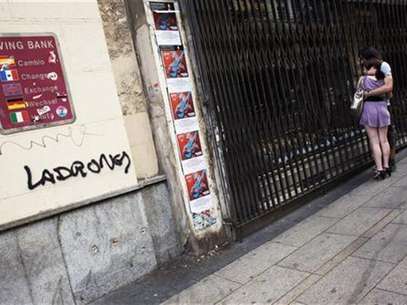 A couple looks at the window of a closed store next to graffiti that reads "Thieves" on the wall of the savings bank Cajastur in Madrid June 11, 2012. Foto: Susana Vera / Reuters In English