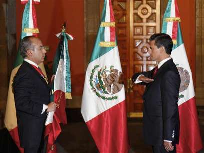 Mexico's outgoing President Felipe Calderon (L) holds the national flag as Mexico's new President Enrique Pena Nieto salutes during a midnight handover ceremony at the Palacio Nacional in Mexico City December 1, 2012. Foto: Presidencia de Mexico / Reuters