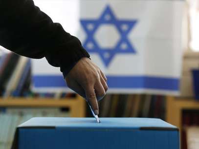 An Israeli flag is seen in the background as a man casts his ballot for the parliamentary election at a polling in the West Bank Jewish settlement of Ofra, north of Ramallah January 22, 2013. Foto: Baz Ratner / Reuters