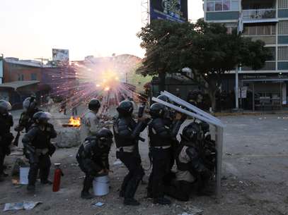 Oficiais da Polícia Nacional Bolivariana se protegem da explosão de um artifício lançado por manifestantes anti-governo durante confrontos em Caracas, em 5 de março Foto: AP