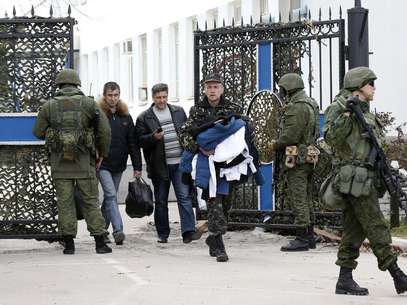 Ucranianos carregam seus pertences passando ao lado de soldados russos na base naval de Sebastopol Foto: Reuters