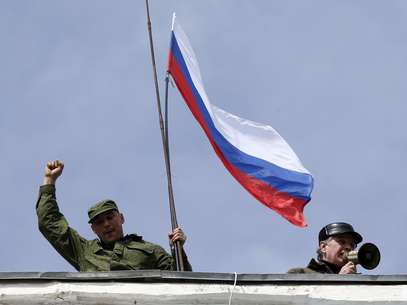 Homem segura uma bandeira russa no telhado da base naval de Sebastopol nesta quarta-feira Foto: Reuters