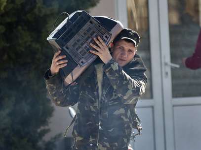 Soldado ucraniano carrega uma televisão enquanto deixa a base militar de Belbek, perto de Sebastopol, Crimeia, nesta sexta-feira Foto: AP