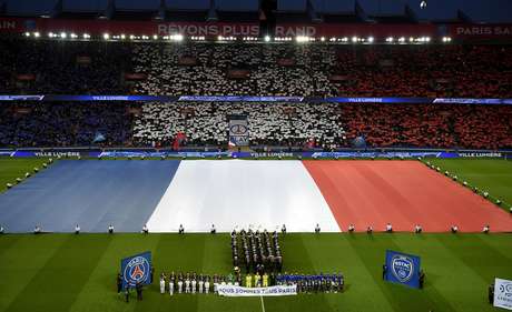 Una bandera francesa gigante es desplegada en la cancha mientras espectadores y jugadores sostienen un cartel que dice "Todos somos París" y guardan un minuto de silencio en honor a las víctimas de los ataques del 13 de noviembre, antes de un partido de la liga francesa entre el Paris Saint Germain y Troyes el sábado, 28 de nov8iembre del 2015, en el Parc des Princes en París.