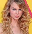 A cantora Taylor Swift usa cachos largos com franjão jogado para o lado   Foto: Shutterstock