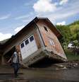 <p>Uma mulher caminha perto de uma casa inclinada por inunda&ccedil;&otilde;es na vila de Krupanj, a oeste de Belgrado, em 19de &nbsp;maio</p>  Foto: Reuters