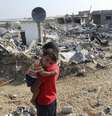  Menino palestino carrega o irmão no colo em frente aos destroços da casa da família em Gaza, em 13 de agosto  Foto: Ibraheem Abu Mustafa / Reuters