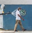 Homem passa pela frente de um grafite, enquanto um funcionário do serviço de saúde borrifa um spray contra o coronavírus. 12/6/2020. REUTERS/Sergio Moraes  Foto: Reuters