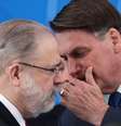 O presidente Jair Bolsonaro cobre a boca e fala algo no ouvido do PGR Augusto Aras  Foto: Reuters / BBC News Brasil