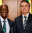 A imagem mostra Sergio Camargo, à esquerda e Jair Bolsonaro, à direita de pé e sorrindo. Eles vestem terno e gravata escuros  Foto: Reprodução/Twitter / Alma Preta