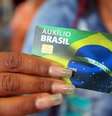 A foto mostra uma mulher negra segurando o cartão do Auxílio Brasil  Foto: Júlio Dutra/ Min. Cidadania / Alma Preta