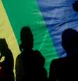 Imagem mostra sombra de pessoas em bandeira LGBTQIAP+.  Foto: Imagem: Pau Barrena/AFP / Alma Preta