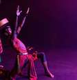 Imagem foca em dois homens negros em trajes vermelhos performando no palco.  Foto: Alma Preta