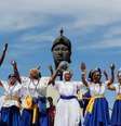Na imagem, mulheres negras com vestimentas azul e branca, em frente a monumento de Zumbi dos Palmares  Foto: Alma Preta