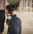 Imagem mostra uma menina negra e pequena, com uma mochila nas costas, abraçada ao braço de uma mulher adulta.  Foto: Alma Preta