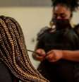 A imagem mostra uma mulher negra retinta fazendo tranças no cabelo de outra mulher.  Foto: Alma Preta