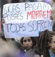 A imagem mostra uma mulher segurando um cartaz com os dizeres “ricas pagam, pobres morrem e todas sofrem” em protesto.  Foto: Alma Preta