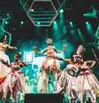 A imagem mostra uma apresentação do Bloco Afro Ilú Obá De Min, com pessoas usando pernaltas e roupas de orixás.  Foto: Alma Preta