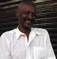 Imagem mostra Seu Carlão do Peruche, um idoso negro com uma camisa social branca.  Foto: Alma Preta