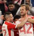 Harry Kane, Jamal Musiala e Raphaël Guerreiro comemorando o gol do Bayern de Munique.   Foto: Alexander Hassenstein/Getty Images / Esporte News Mundo
