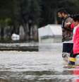 homem ajudando mulher a andar por rua alagadaágua  Foto: Reuters / BBC News Brasil