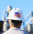 Homem com capacete de trabalho que tem bandeira dos EUA; ele observa planta industrial  Foto: Getty Images / BBC News Brasil