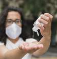 Mulher com máscara de proteção usando álcool em gel nas mãos.  Foto: Freepik