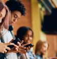 Quatro alunos de pé contra uma parede de tijolos, sem falar uns com os outros enquanto cada um olha para um telefone em suas mãos  Foto: Getty Images / BBC News Brasil