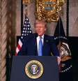O presidente Donald Trump fala com repórteres de um púlpito com o selo do presidente dos EUA. Uma bandeira americana e uma bandeira com o selo do presidente estão atrás dele. Ele veste um terno escuro e uma gravata azul  Foto: Getty Images / BBC News Brasil