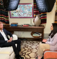 O príncipe Harry está sentado em um sofá branco na sala de estar, em frente a Nada Tawfik que está sentada em um sofá laranja listrado. O equipamento de iluminação da TV pode ser visto acima de suas cabeças.  Foto: BBC News Brasil
