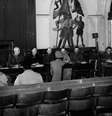 Uma mulher alemã, que acusa três soldados norte-americanos de estupro, presta depoimento diante de oficiais superiores em uma prefeitura na Alemanha. Atrás dela, há uma pintura que mostra soldados da Wehrmacht, do Volkssturm e da Juventude Hitlerista empunhando bandeiras. Esse foi o primeiro julgamento por corte marcial da história da 7ª Divisão do Exército dos Estados Unidos realizado em solo alemão.  Foto: Getty Images - Horace Abrahams / RFI