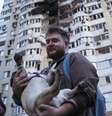 Um homem carrega seu cachorro em frente a um prédio residencial de vários andares danificado após um ataque de drone russo em Kiev, Ucrânia, nesta sexta-feira  Foto: AP - Evgeniy Maloletka / RFI