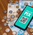 Celular com tela mostrando Pix e notas e moedas de real ao fundo  Foto: Getty Images / BBC News Brasil