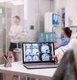 Senior woman in hospital office looking at brain ct  Foto: scan while discussing with doctor about diagnosis. Sick young woman and elderly medic with grey hair in clinic corridor. / Revista Malu