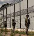 Soldados de fronteira armados montam guarda frente a uma alta e longa barreira metálica com concertinas de arame farpado  Foto: Getty Images / BBC News Brasil