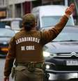 Uma policial chilena vista de costas vestindo uniforme marrom com colete a prova de balas onde se lê "Carabineros de Chile". Ela tem o braço direito erguido e faz sinal para veículos na rua desviarem  Foto: Getty Images / BBC News Brasil