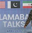 Um guarda paquistanês, vestindo um uniforme de camuflagem, passa por um outdoor sobre as negociações de paz entre os EUA e o Irã em Islamabad  Foto: Farooq Naeem / AFP via Getty Images / BBC News Brasil