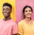 Um homem e uma mulher jovens aparecem lado a lado diante de uma parede pintada com cores vibrantes. Ele veste uma camiseta rosa diante de uma parte amarela da parede, enquanto ela usa uma camiseta amarela diante de uma área rosa  Foto: Getty Images / BBC News Brasil