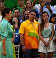 Michelle aparece em primeiro plano, desfocada, em vestido verde e falando ao microfone em um comício eleitoral de 2022. Ao fundo, Flávio e sua esposa observam Michelle ao lado de outras pessoas  Foto: MAURO PIMENTEL/AFP via Getty Images / BBC News Brasil