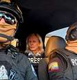 Dois policiais equatorianos com óculos de sol, capacetes e balaclavas, sentados em um carro com a jornalista da BBC Orla Guerin na parte de trás, vestindo uma jaqueta com a palavra 'IMPRENSA' em inglês  Foto: Lee Durant/BBC / BBC News Brasil