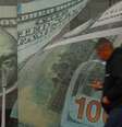 Um homem passa em frente a uma casa de câmbio, com adesivos de notas de dólar na porta e nas paredes  Foto: Reuters