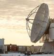 A Base Espacial Pituffik (antiga Base Aérea de Thule) é mostrada no norte da Groenlândia, em 4 de outubro de 2023. A imagem mostra uma grande antena parabólica em frente a contêineres, com um céu alaranjado e nublado ao fundo. Foto: Thomas Traasdahl/Ritzau Scanpix/AFP via Getty Images / BBC News Brasil