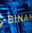 O logotipo da Binance, que sofreu um ataque hacker,  em contraste com um texto azul desfocado, típico de computador.  Foto: Reuters / BBC News Brasil