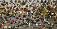 Cadeados que casais apaixonados prendem nas grades de uma ponte sobre o rio Sena  Foto: Reuters