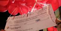 Imagem mostra o cheque sendo erguido por balões vermelhos  Foto: EFE