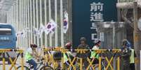 Estudantes passam de bicicleta por guardas em uma ponte em Paju, na Coreia do Sul  Foto: AP