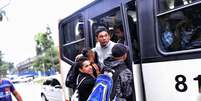 Homens se arriscam e pegam ônibus pendurados na porta traseira  Foto: Fernando Borges / Terra