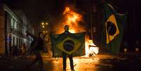 <p>Mascarado, manifestante mostra a bandeira do Brasil em frente a uma barricada de lixo em chamas no Rio de Janeiro</p>  Foto: AP