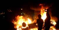 Jovens são vistos em frente ao carro queimado na noite de segunda-feira  Foto: Mauro Pimentel / Terra